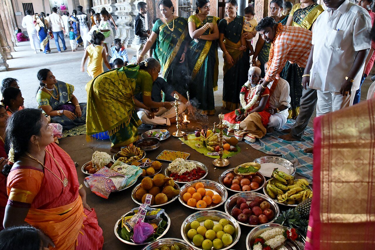 a traditional South Indian family ceremony, likely a Valaikappu (baby shower), puberty ceremony (Manjal Neerattu Vizha), or ritual offering featuring elaborate plates of ritual items, fruits, sweets, and floral arrangemen