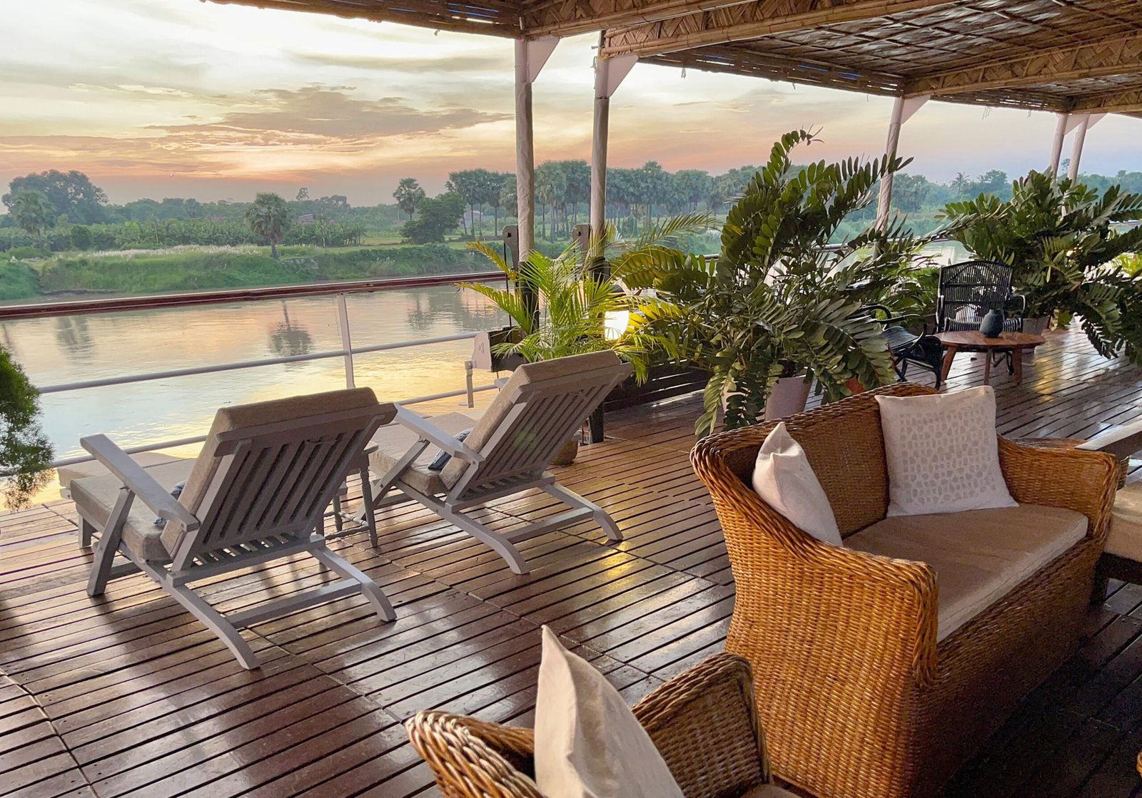 Canopied sundeck of ABN Rajmahal at sunset with loungers and wicker sofas on a Hooghly river cruise